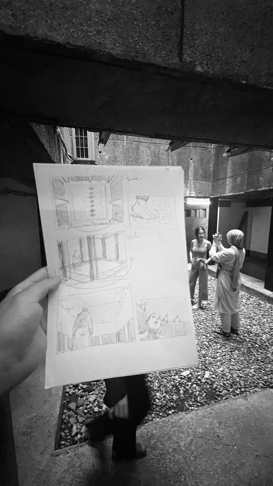 A pencil storyboard held up against the courtyard it was drawn for