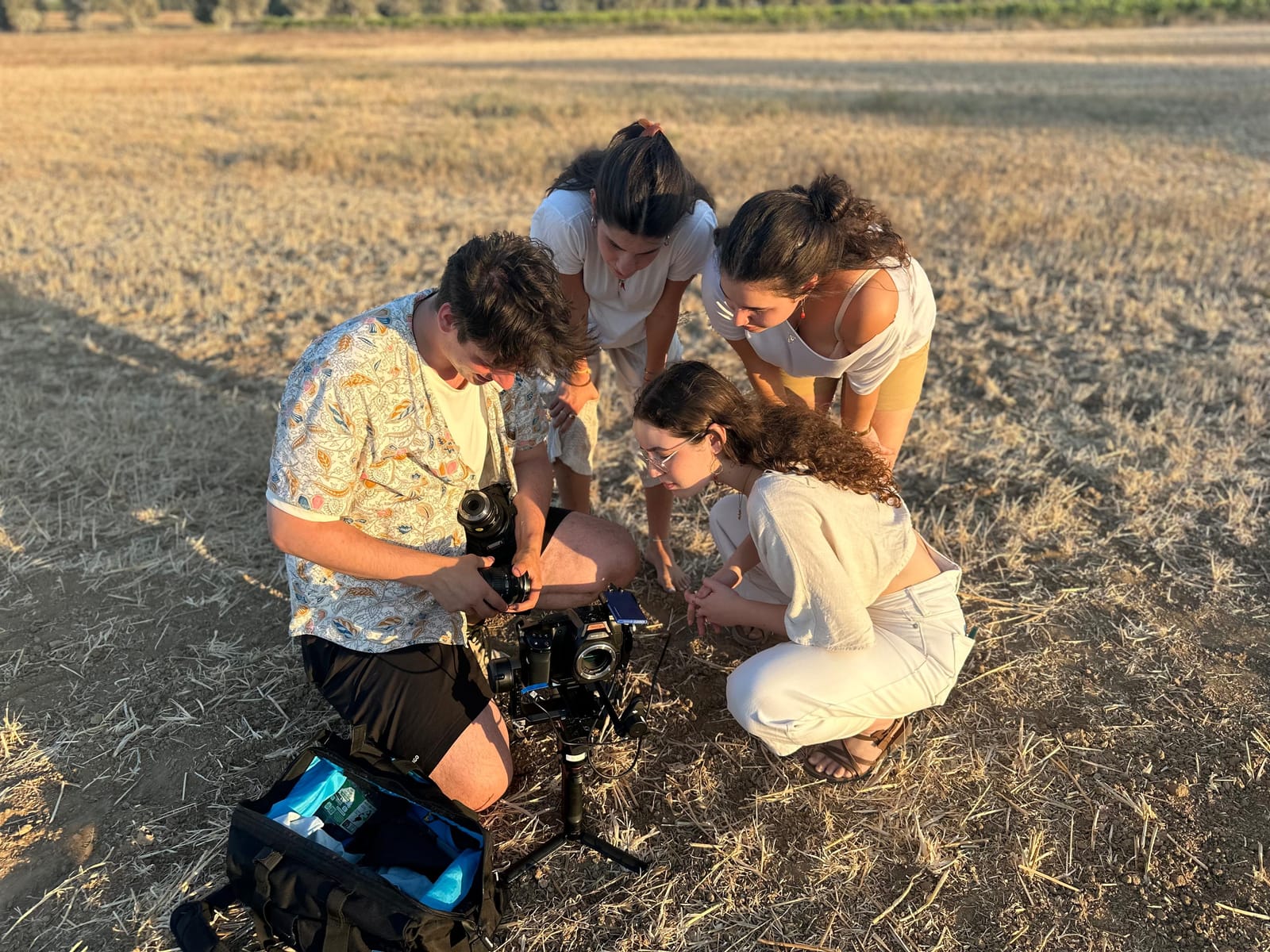 Crew crouched around a camera monitor in a dry field at golden hour