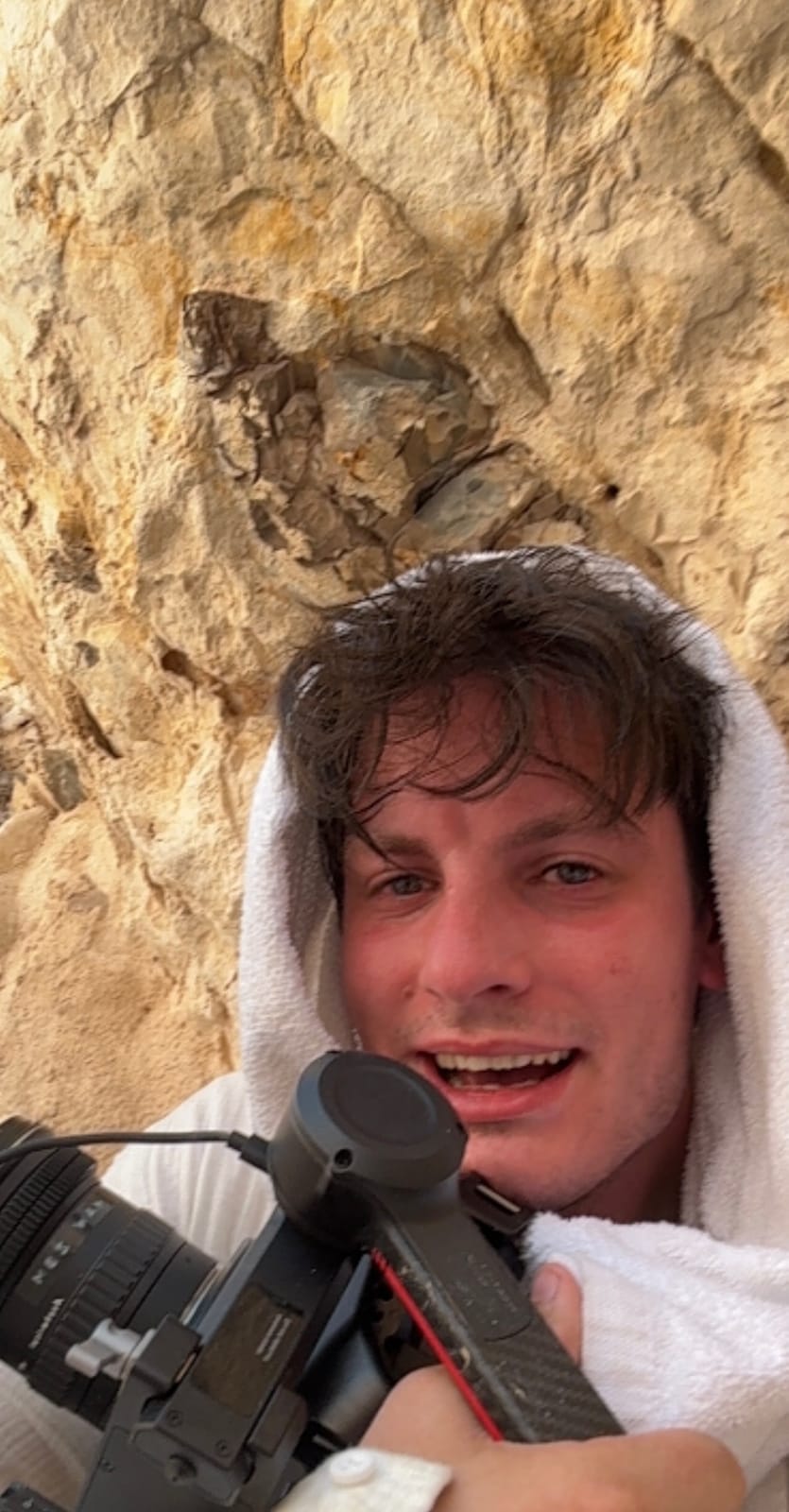 Selfie wrapped in a towel with the camera rig, in front of a rock face