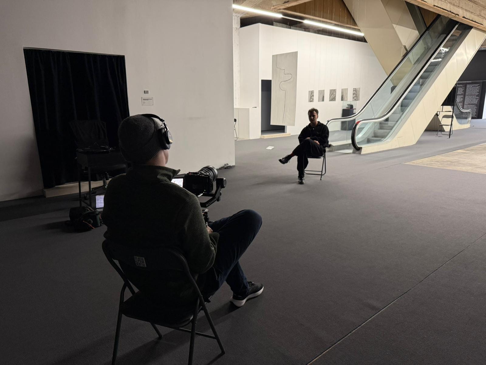 Interview setup in an empty exhibition hall, camera facing the seated guest