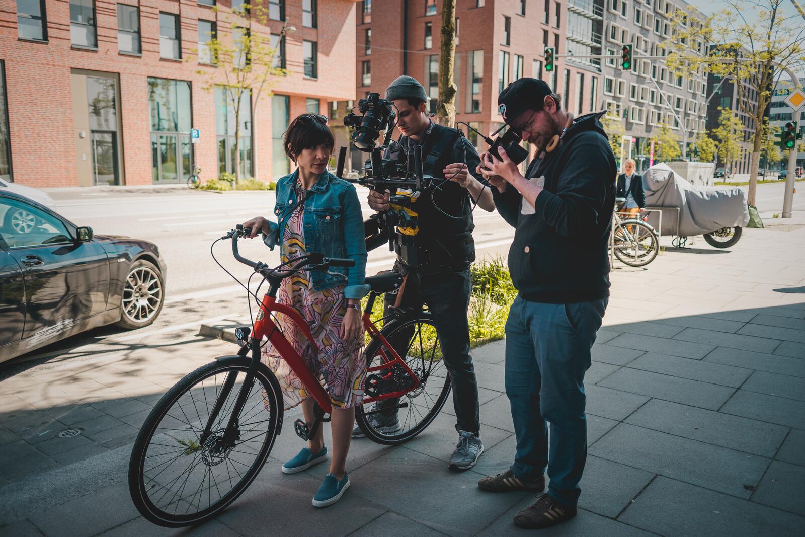 Two camera operators setting up a shot with a woman and her bicycle on a city street