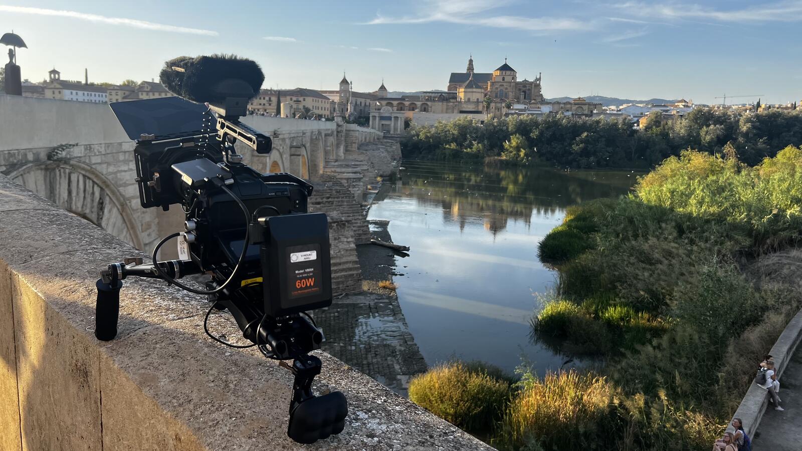 Cinema camera with a furry windshield on a bridge parapet, looking over a river towards an old town
