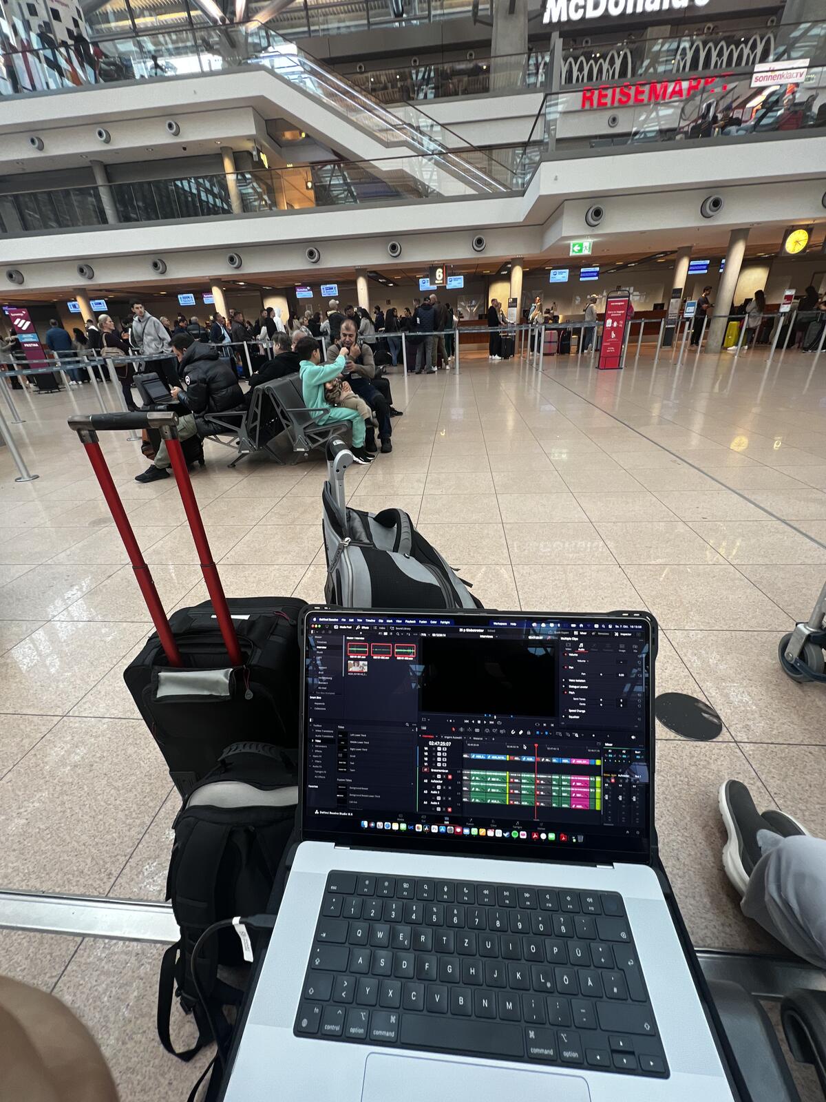 Editing on a laptop balanced on camera cases in an airport departure hall