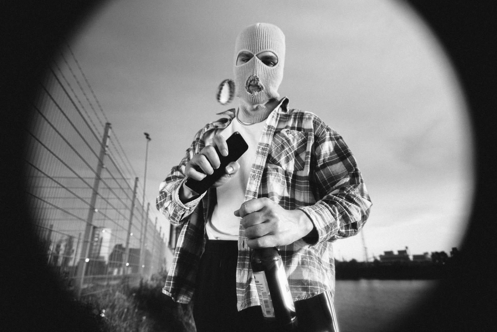 Fisheye portrait of a man in a balaclava holding a bottle, in black and white