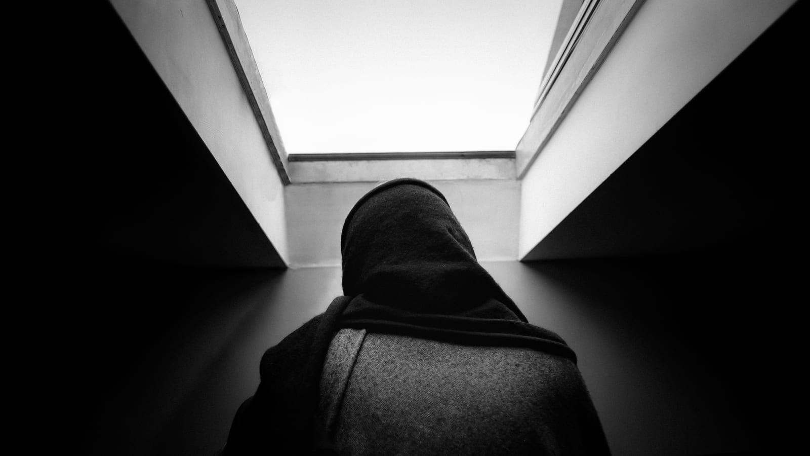 Hooded figure beneath a skylight, in black and white