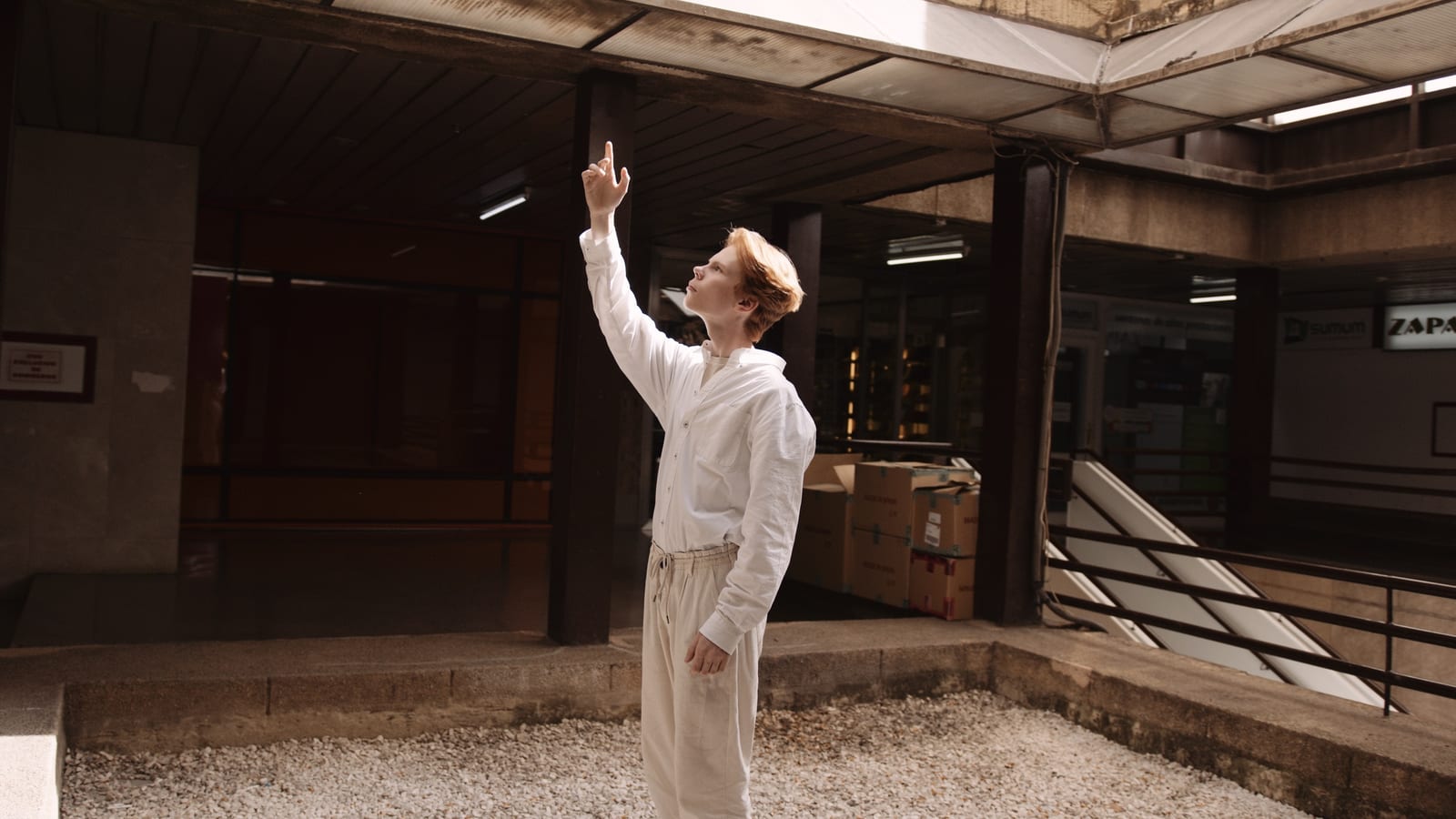 Performer in white pointing upward inside an abandoned building