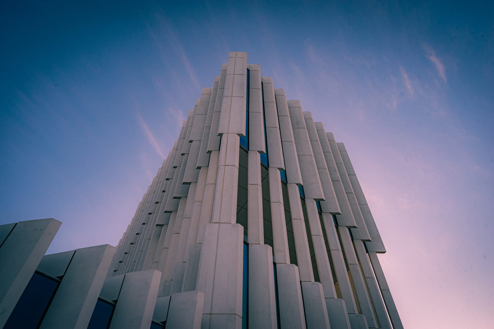 Low-angle view of a ribbed tower against a pink dusk sky
