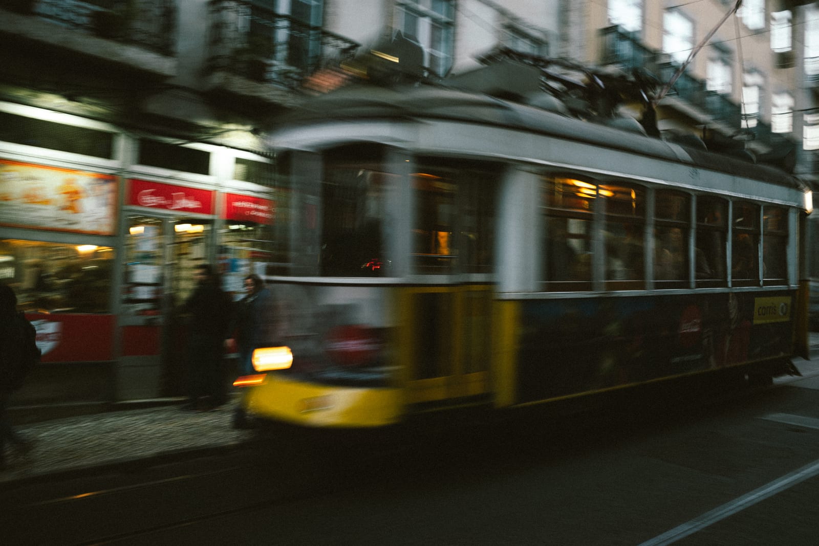 Yellow tram passing through a busy street at dusk